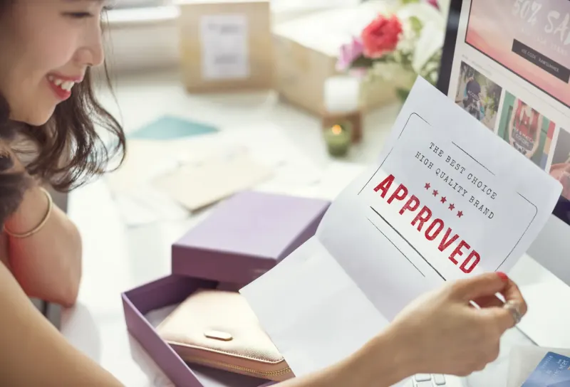 Smiling woman at her desk holding up a card stamped “Approved”
